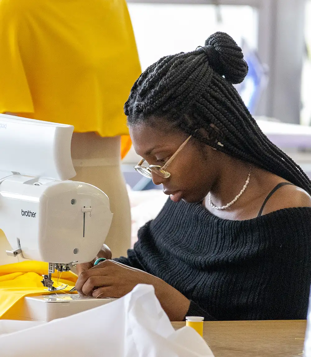 Student using a sewing machine to stitch bright yellow fabric in a studio.