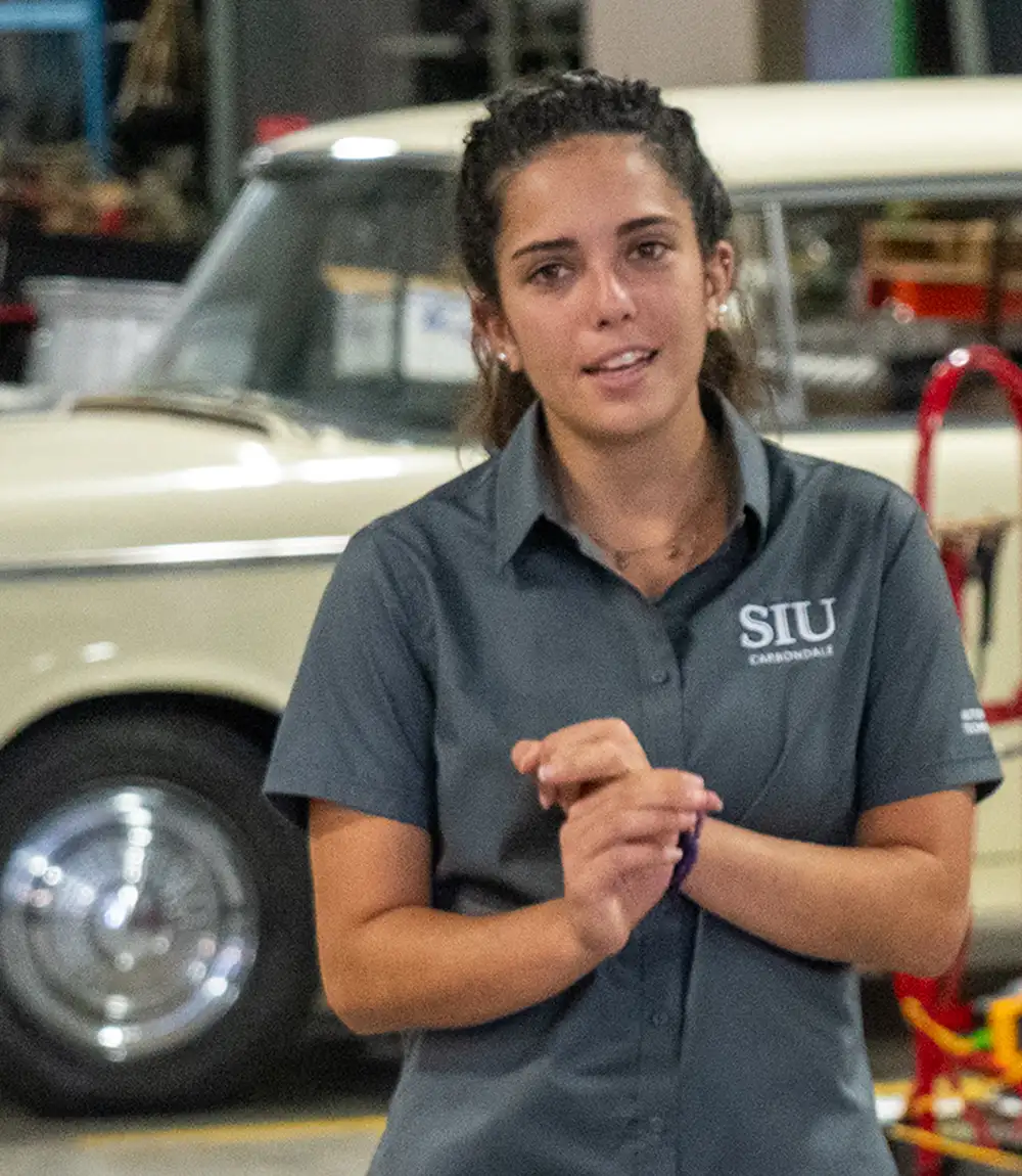 Automotive student standing in a lab with a classic car in the background.