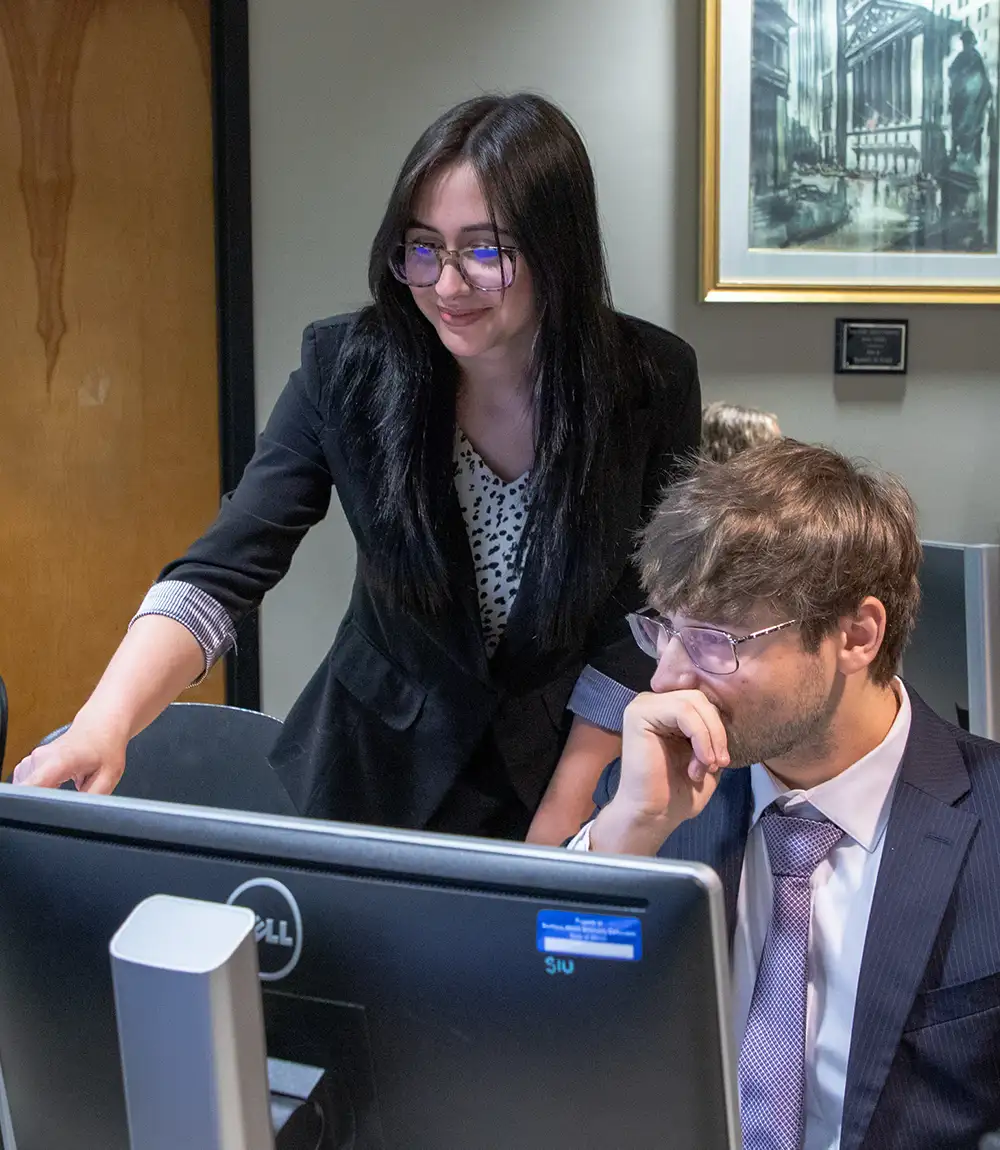 Two students in business attire reviewing information together at a computer.