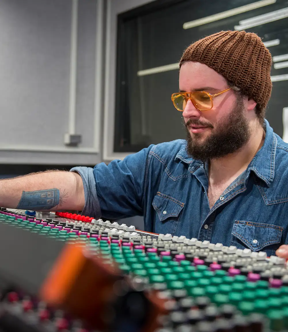 Student adjusting controls on an audio mixing console in a production studio.
