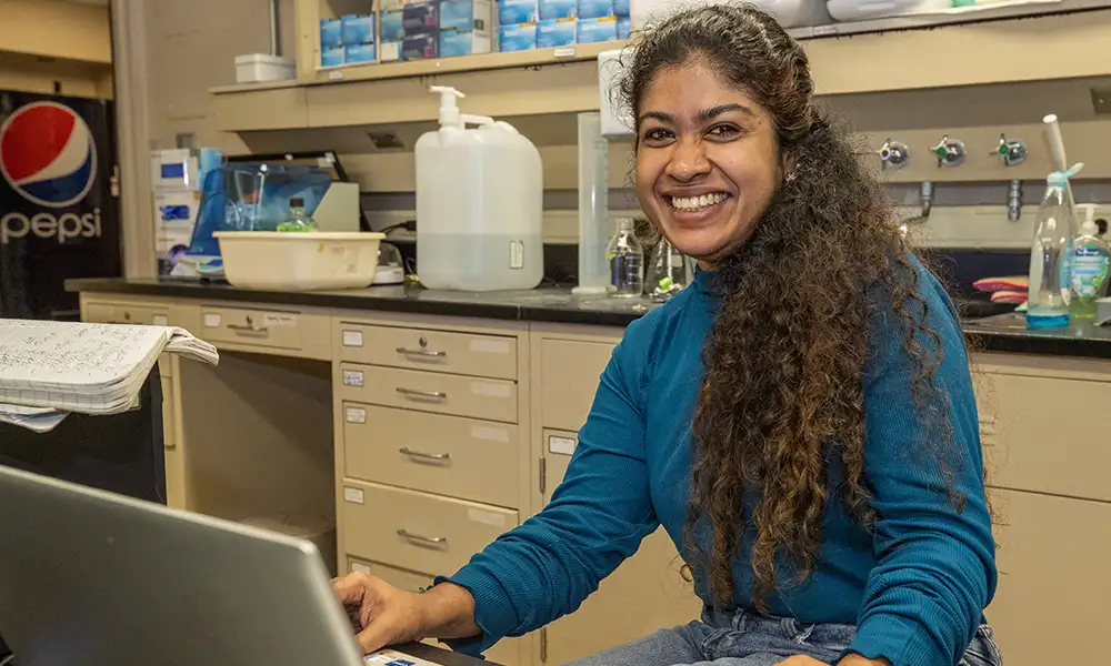 Graduate student working on a laptop in a laboratory setting.