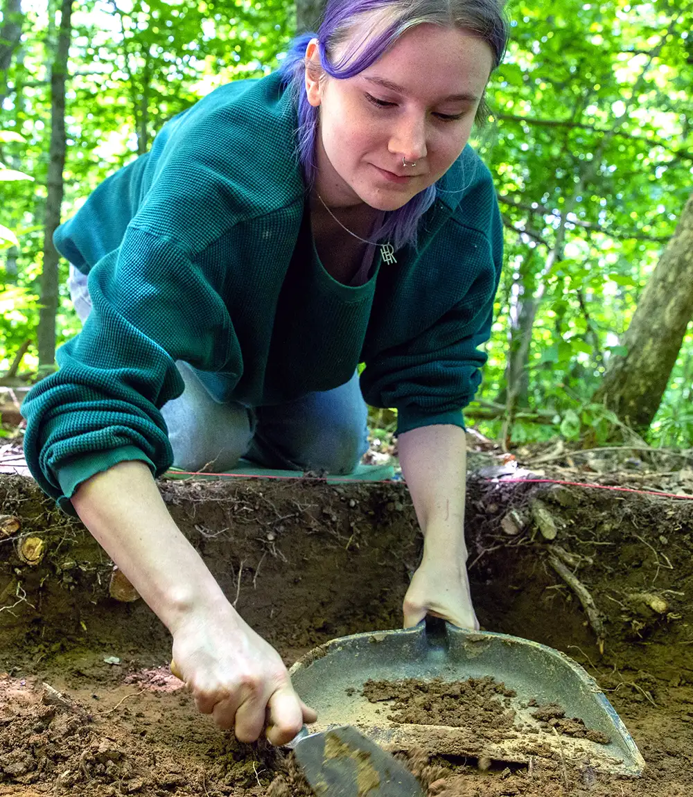 Student conducting soil analysis at an outdoor excavation site.