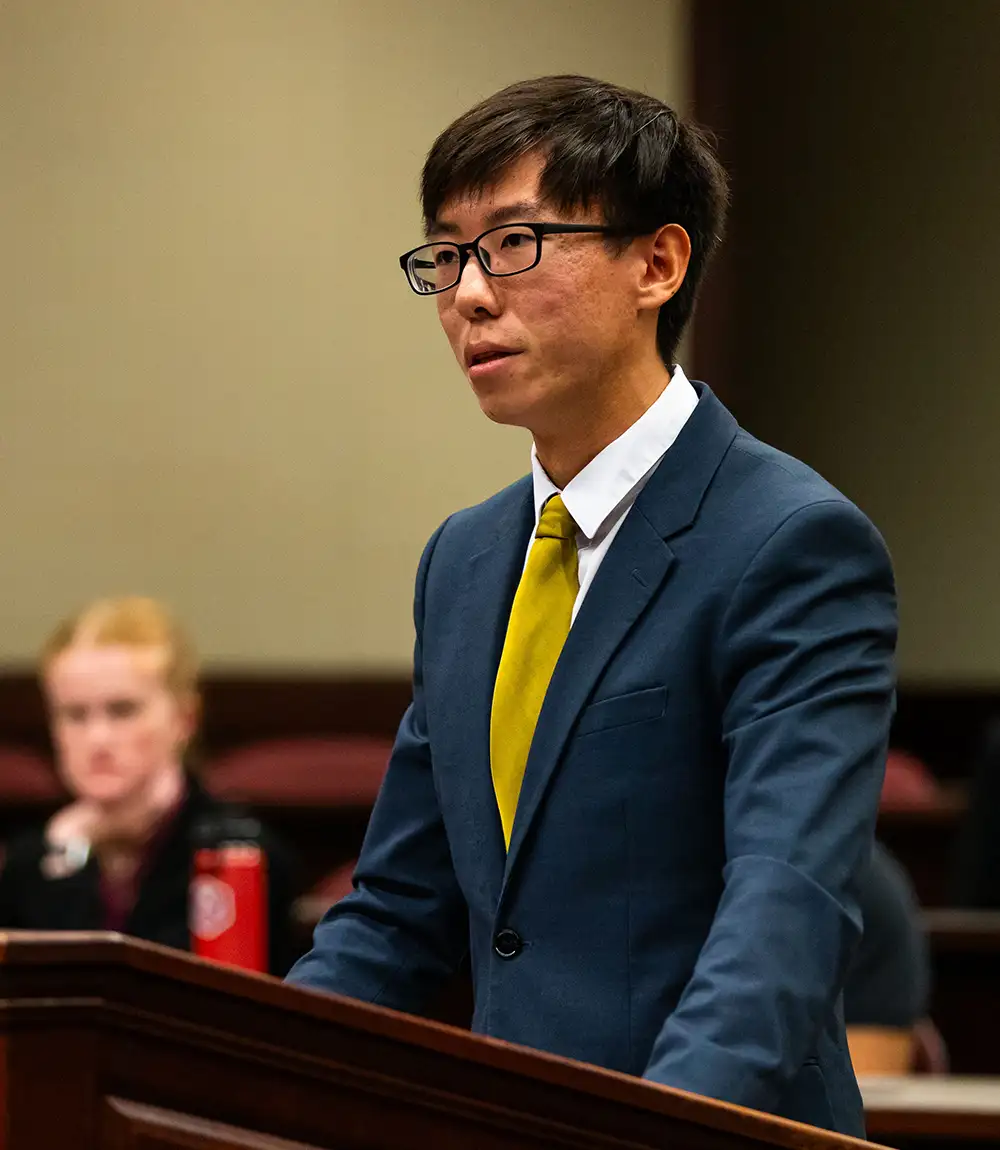 Student speaking at a podium in a courtroom-style classroom.