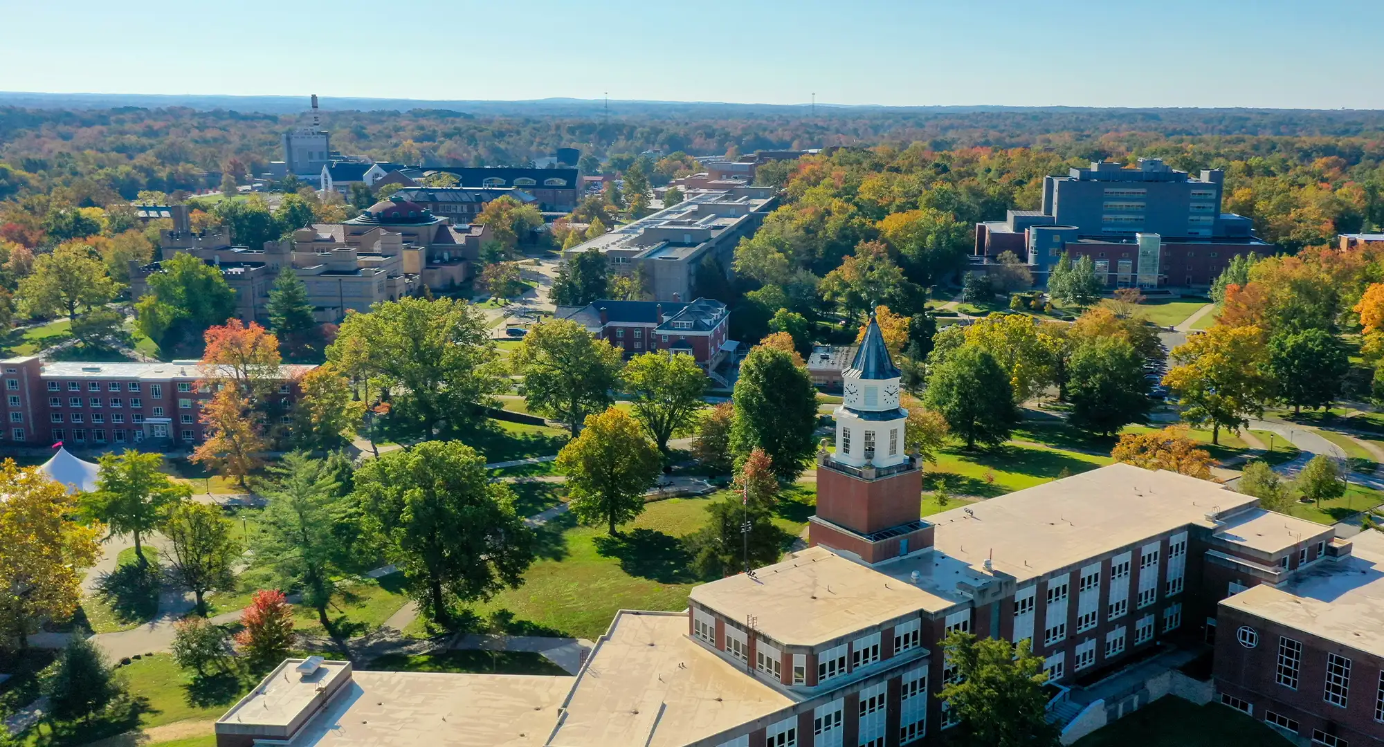 Aerial view of the SIU campus in autumn, with academic buildings, tree-lined walkways, and a prominent clock tower surrounded by colorful fall foliage under a clear blue sky.