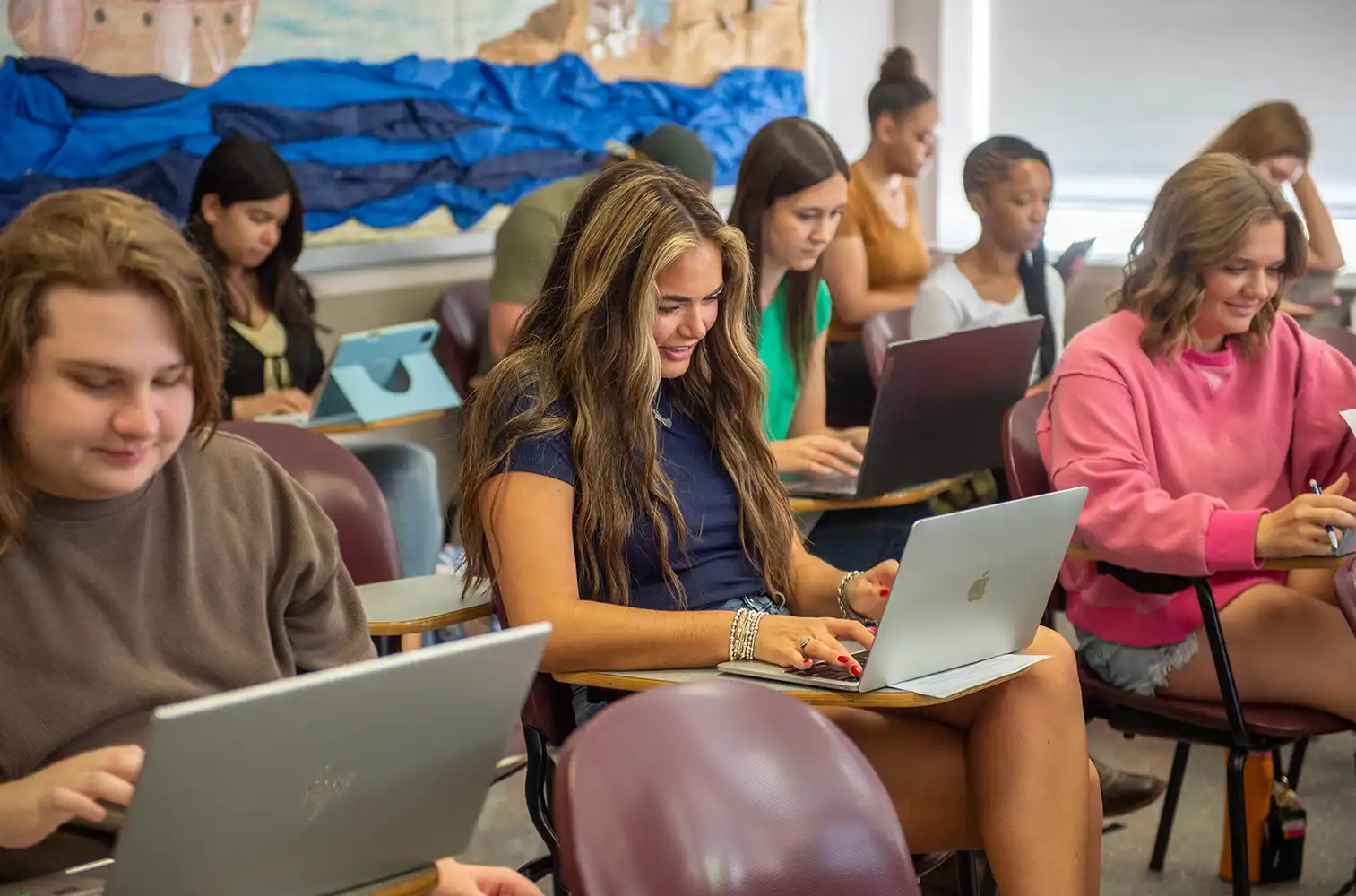 Students seated in a classroom working on laptops during class.