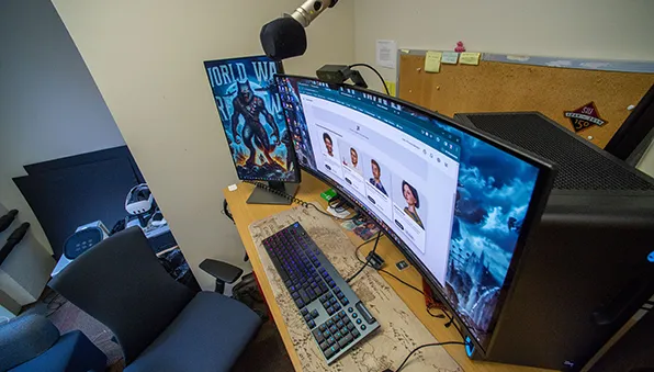 Desk setup with dual monitors displaying a website interface, with a keyboard, mouse, and overhead microphone in an office