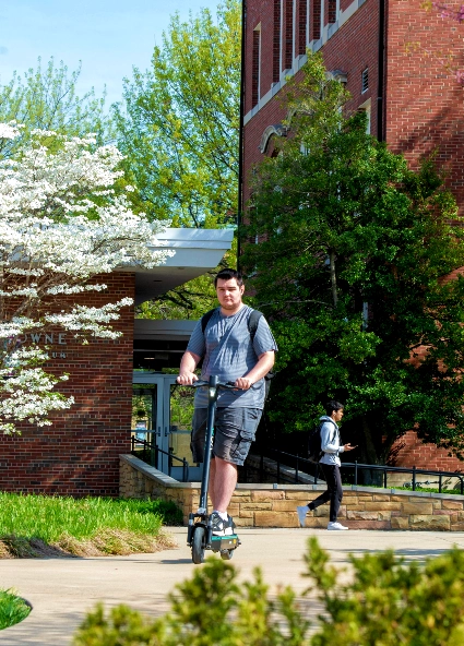 student riding scooter on campus