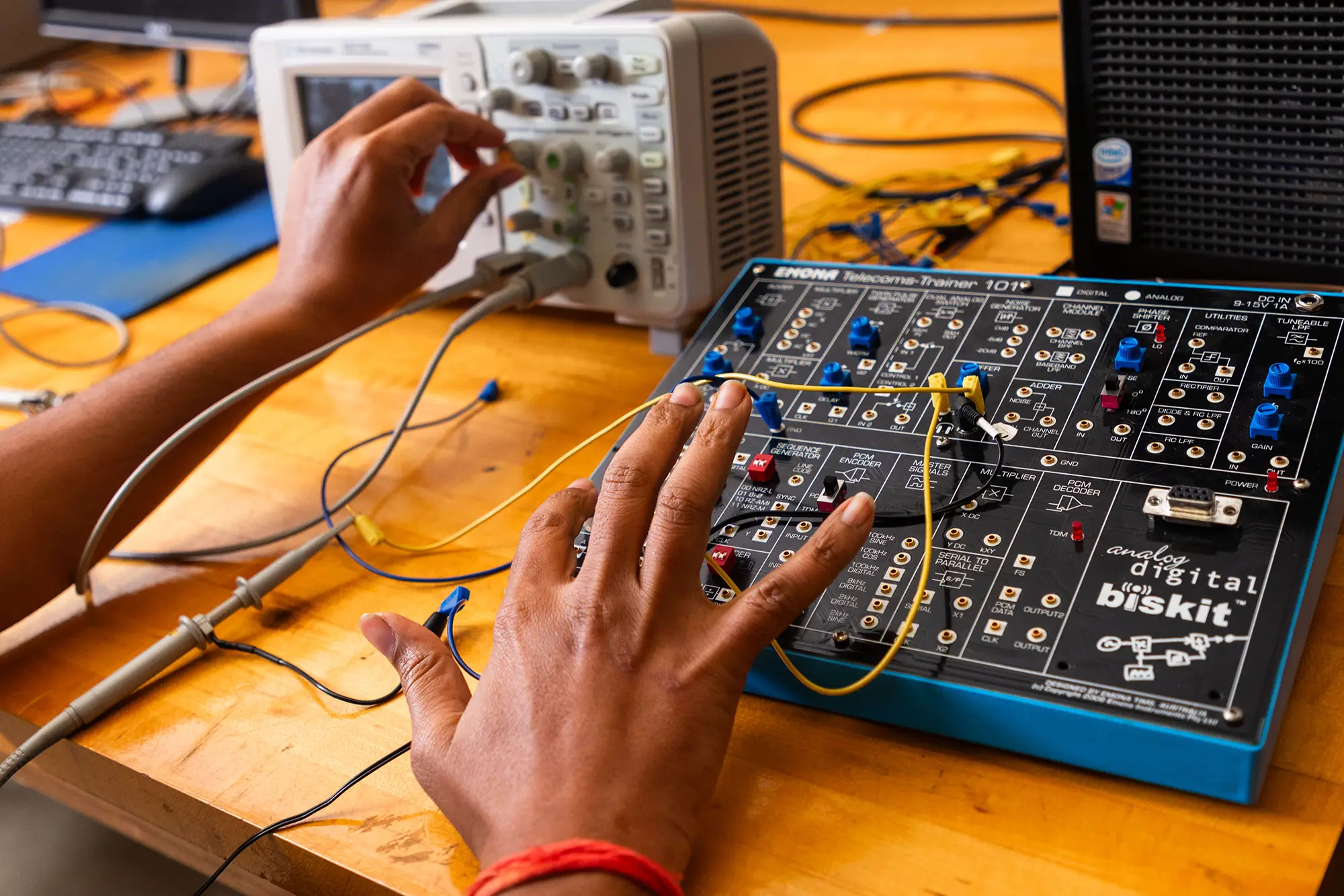 A student works with an Emona Telecoms-Trainer and oscilloscope on a telecommunications electronics lab bench.