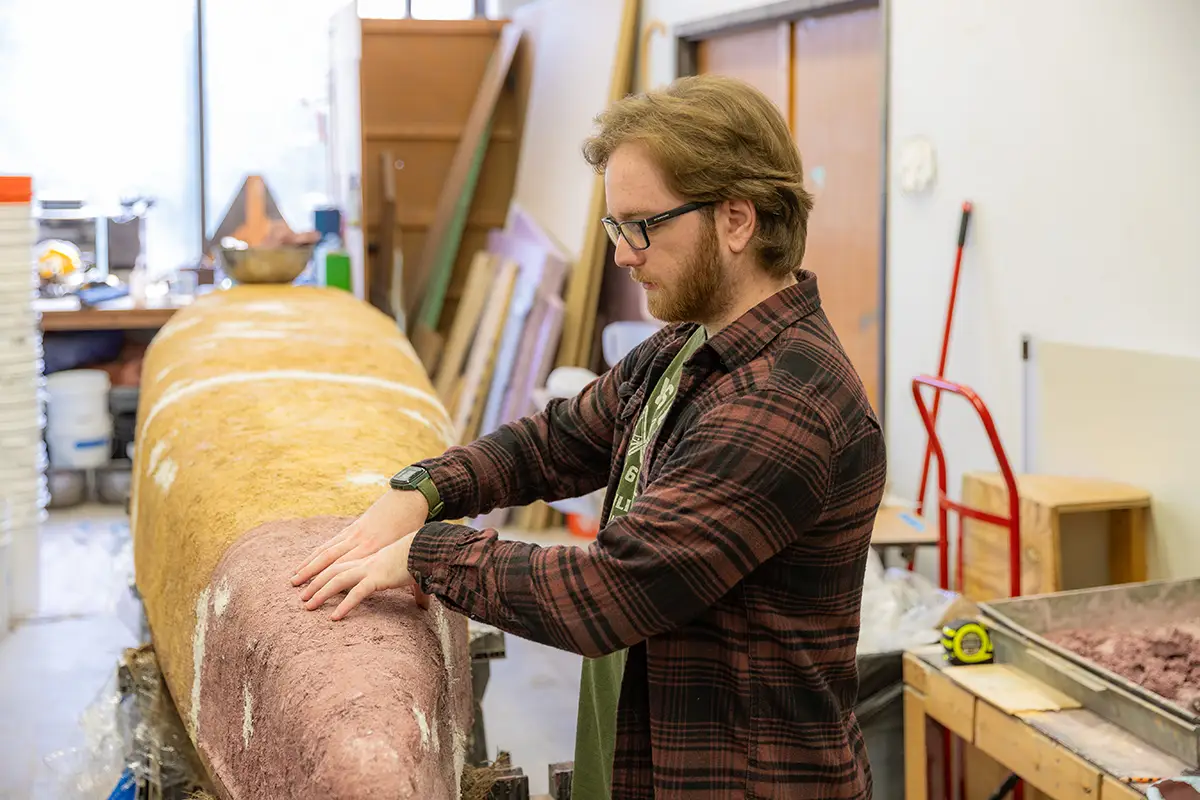 A student works on the hull of a concrete canoe in a campus workshop.