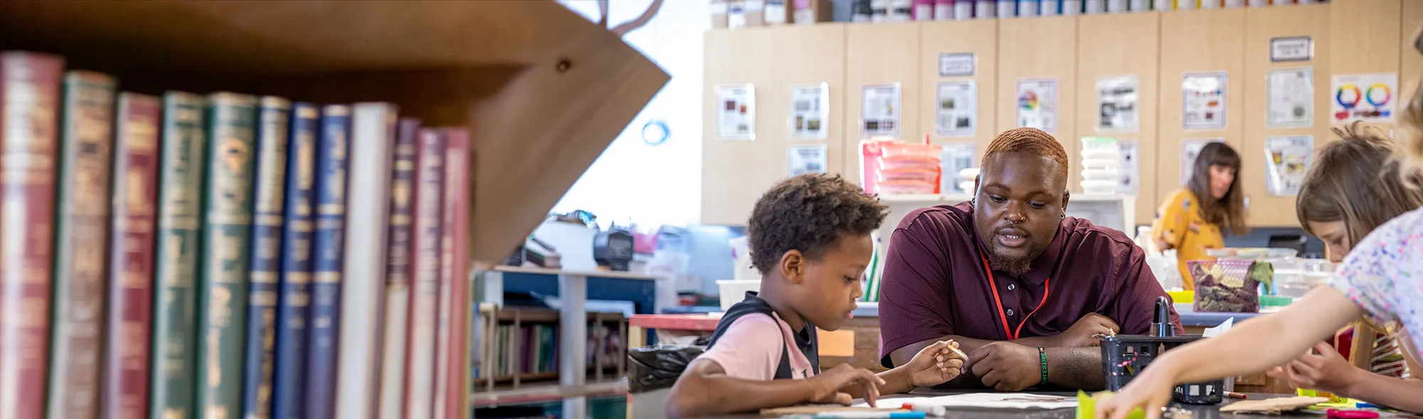 SIU student sits at a table working on an art project with young children in a classroom stocked with art supplies.