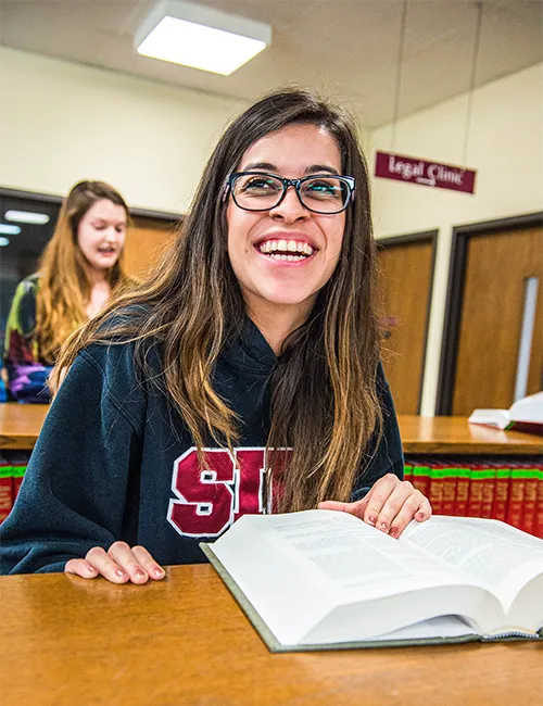 A student in an SIU sweatshirt sits at a table with an open book.